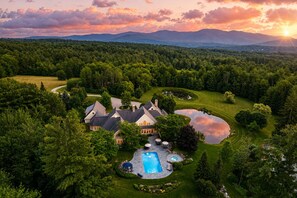 A large house surrounded by a lush forest, with a swimming pool and a tennis court. - “Eden” 8BR Luxury Retreat with Pool, Spa, Concierge near Ski and Trails (Stowe)