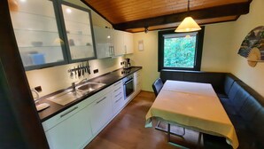 A compact kitchen with a sink, stove, and dining area with a table and bench. - Bungalow in Waldbrunn (Waldbrunn)