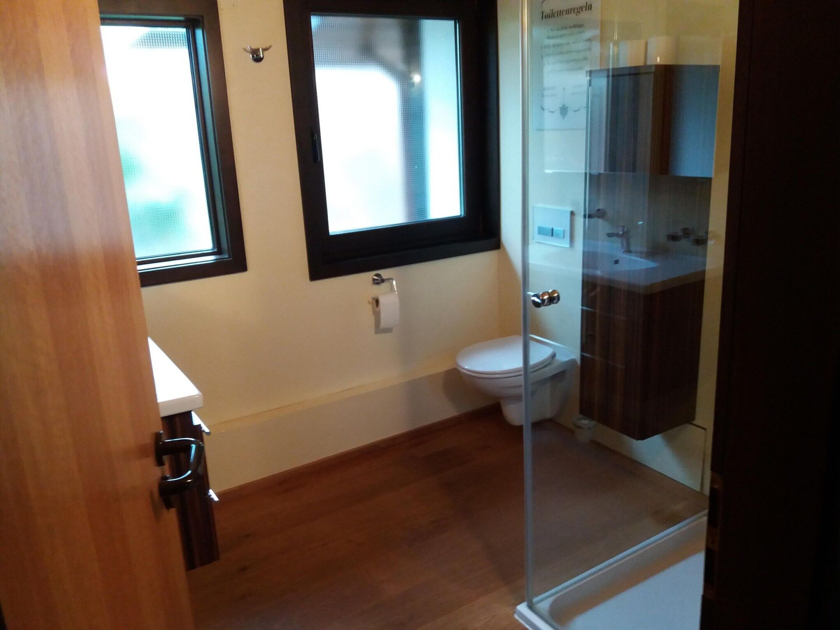 A bathroom with a toilet, a glass shower enclosure, and a window above the toilet.