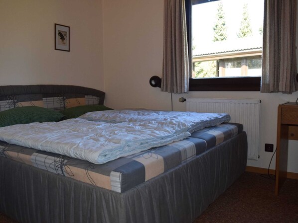 A bedroom with a bed, a window with curtains, a radiator, and a small table. - Bungalow in Waldbrunn (Waldbrunn)