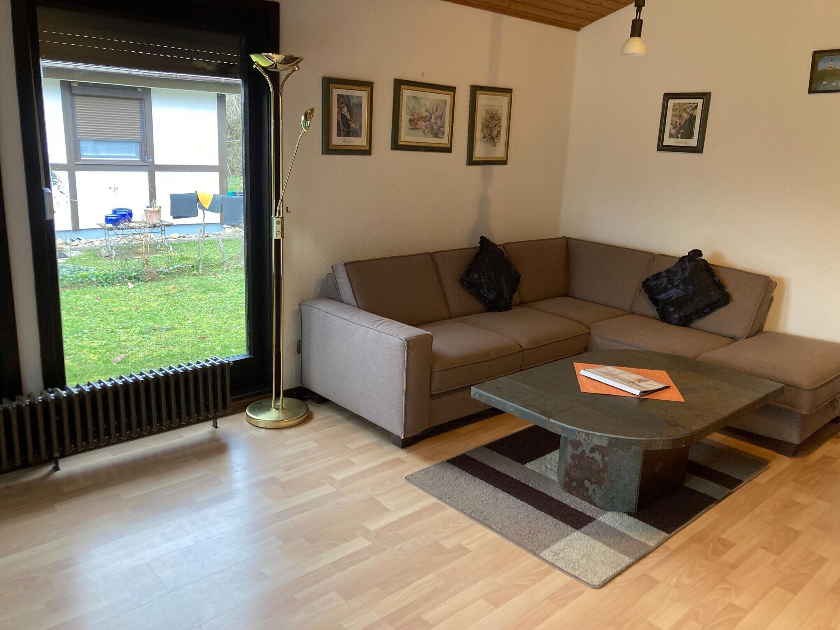 A living room with a sofa, coffee table, floor lamp, and a view of the outside.
