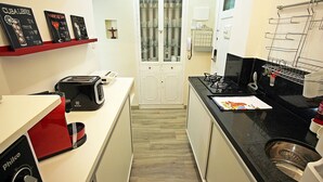 Una cocina compacta con tostadora, cafetera, microondas y pileta. Hay un pequeño armario con puertas de vidrio y una repisa con fotos enmarcadas.