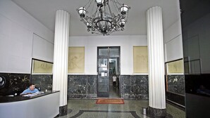 Una zona de recepción con suelo de mármol, una araña y una recepcionista en el mostrador.