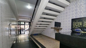 Un pasillo de hotel con una escalera, un mostrador de recepción y un televisor.