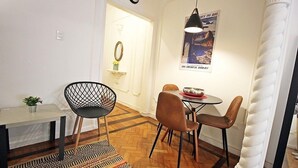 Un área de comedor con una mesa redonda, dos sillas, una lámpara colgante y un tapete estampado.