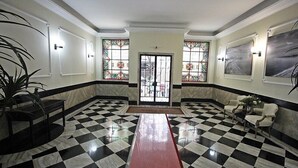 Un vestíbulo con suelo a cuadros, un banco rojo central y dos puertas con vidrieras.