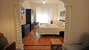 Habitación de hotel con cama, escritorio, silla, televisión y ventana con cortinas.