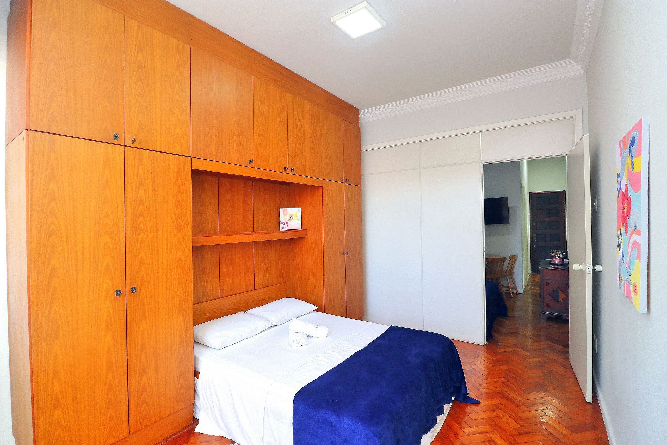 Un dormitorio con un armario de madera, una cama con ropa de cama blanca y un plaid azul.