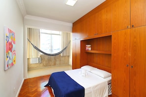 A room with a bed, wooden wardrobe, a hammock, and a window with curtains. - Rio Spot U041 (Rio de Janeiro)