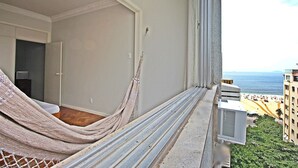 A balcony with a hammock, a window air conditioner, and a view of the sea and buildings. - Rio Spot U041 (Rio de Janeiro)