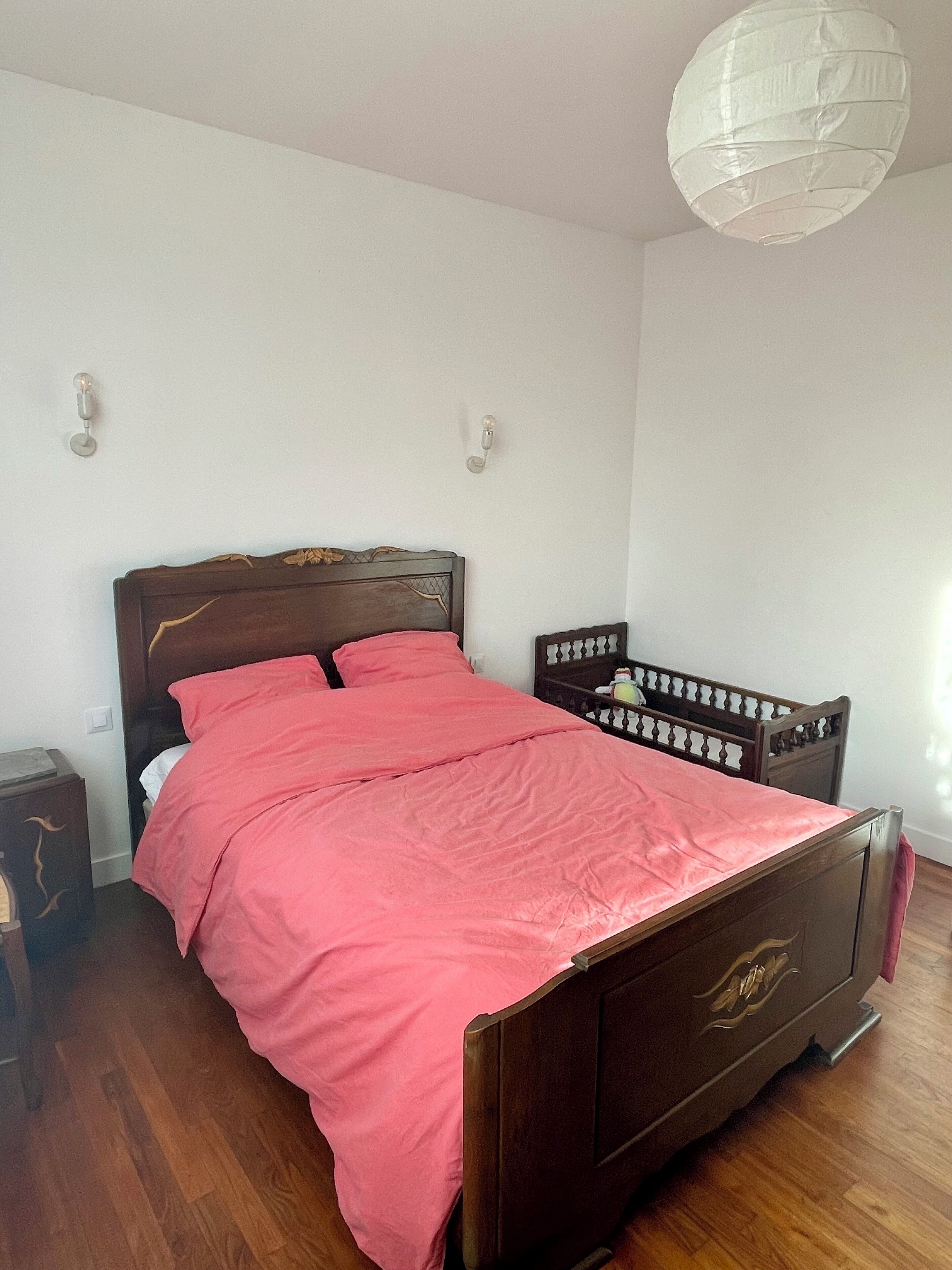 A bedroom with a wooden bed, a red bedspread, and a white ceiling light.