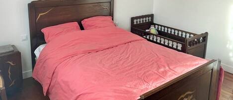 A bedroom with a wooden bed, a red bedspread, and a white ceiling light.