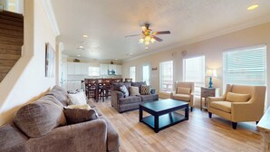 A spacious living room with a sofa set, a coffee table, and a dining area with chairs and a kitchen in the background. - Bellagio: 5  BR, 3.5  BA House in Crystal Beach, Sleeps 18 (Bolivar Peninsula)