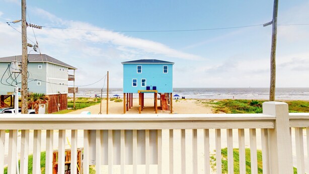 A coastal house with a blue exterior, a wooden deck, and a view of the ocean. - Bellagio: 5  BR, 3.5  BA House in Crystal Beach, Sleeps 18 (Bolivar Peninsula)