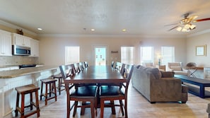 A spacious living area with a long dining table, a sofa, and a kitchen with white cabinets and a microwave. - Bellagio: 5  BR, 3.5  BA House in Crystal Beach, Sleeps 18 (Bolivar Peninsula)