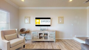 A living room with a beige sofa, a wooden cabinet, and a mounted television. - Bellagio: 5  BR, 3.5  BA House in Crystal Beach, Sleeps 18 (Bolivar Peninsula)