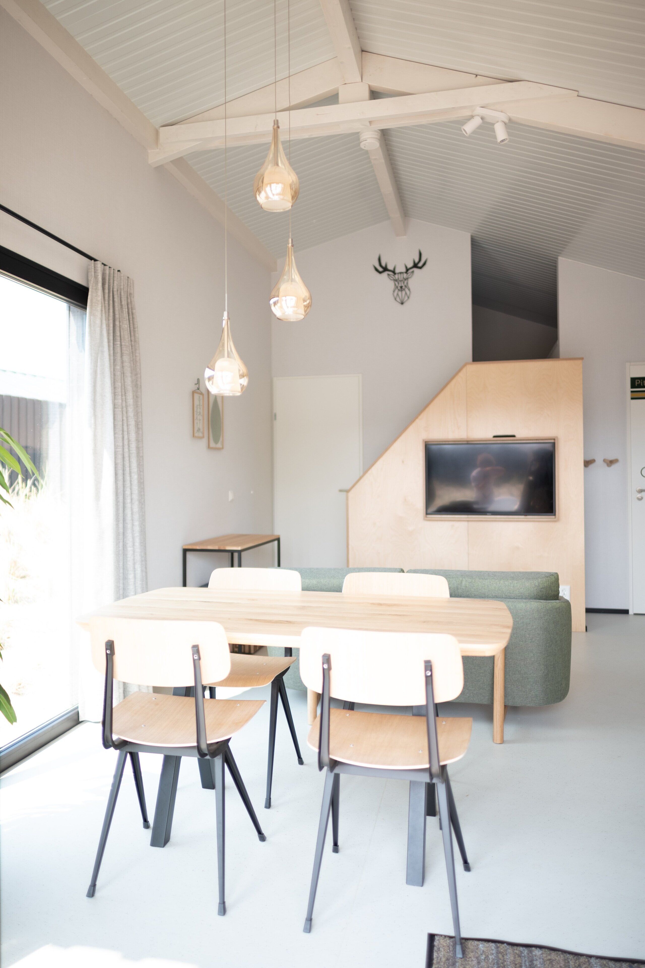 Un intérieur moderne comprenant un coin repas, un canapé, un téléviseur fixé à un mur en bois et un plafond avec des poutres apparentes.