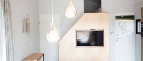 Ein modernes Wohnzimmer mit einer Couch, einem an einer Holzwand befestigten Fernseher und Pendelleuchten.