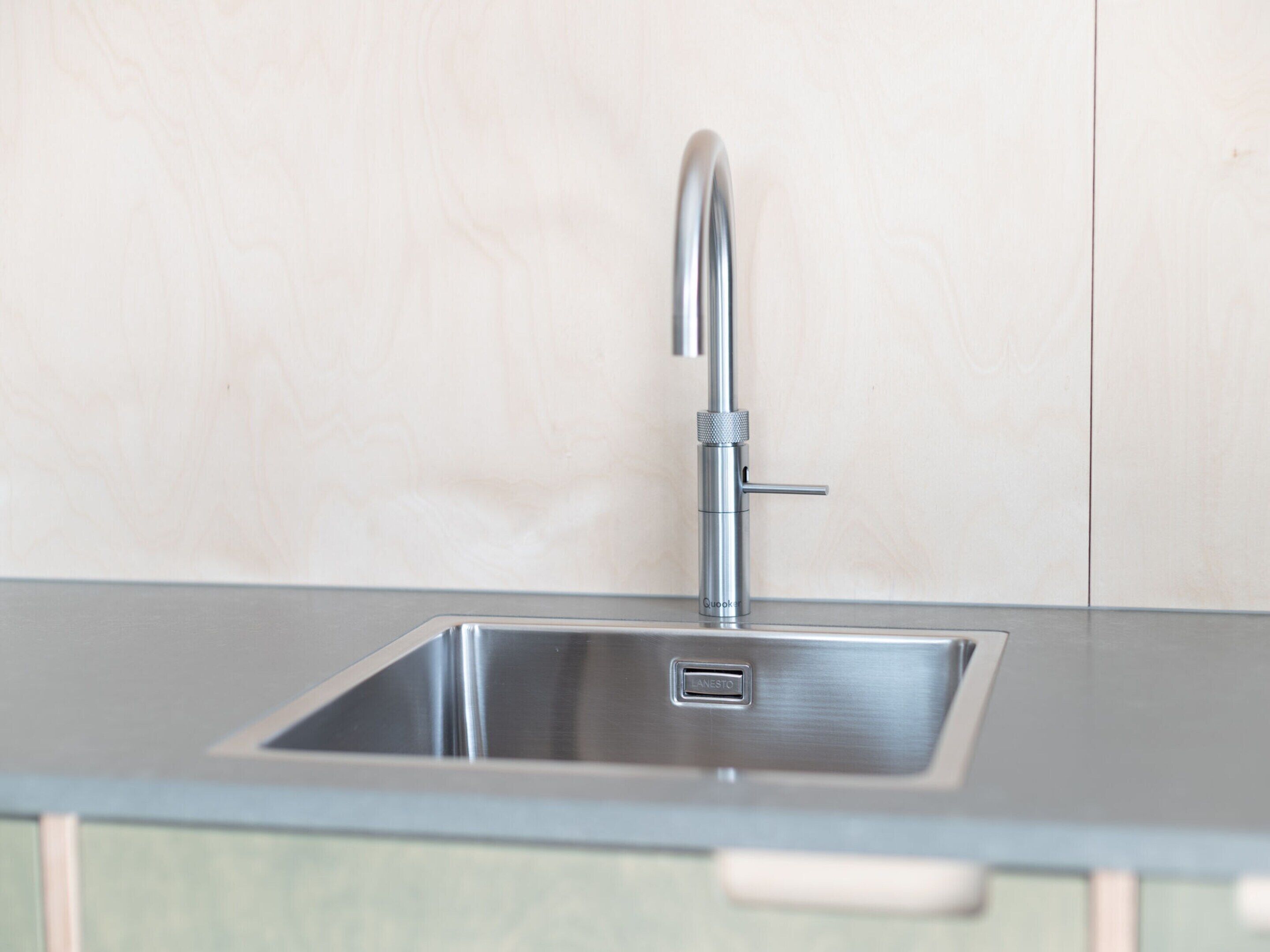 A modern kitchen with a stainless steel sink, a single drawer cabinet, and a neutral-colored backsplash.