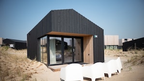 A modern beach house with a wooden deck and white plastic chairs.