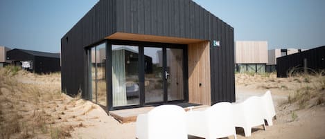 Una casa moderna frente a la playa con una terraza de madera y sillas de plástico blanco.