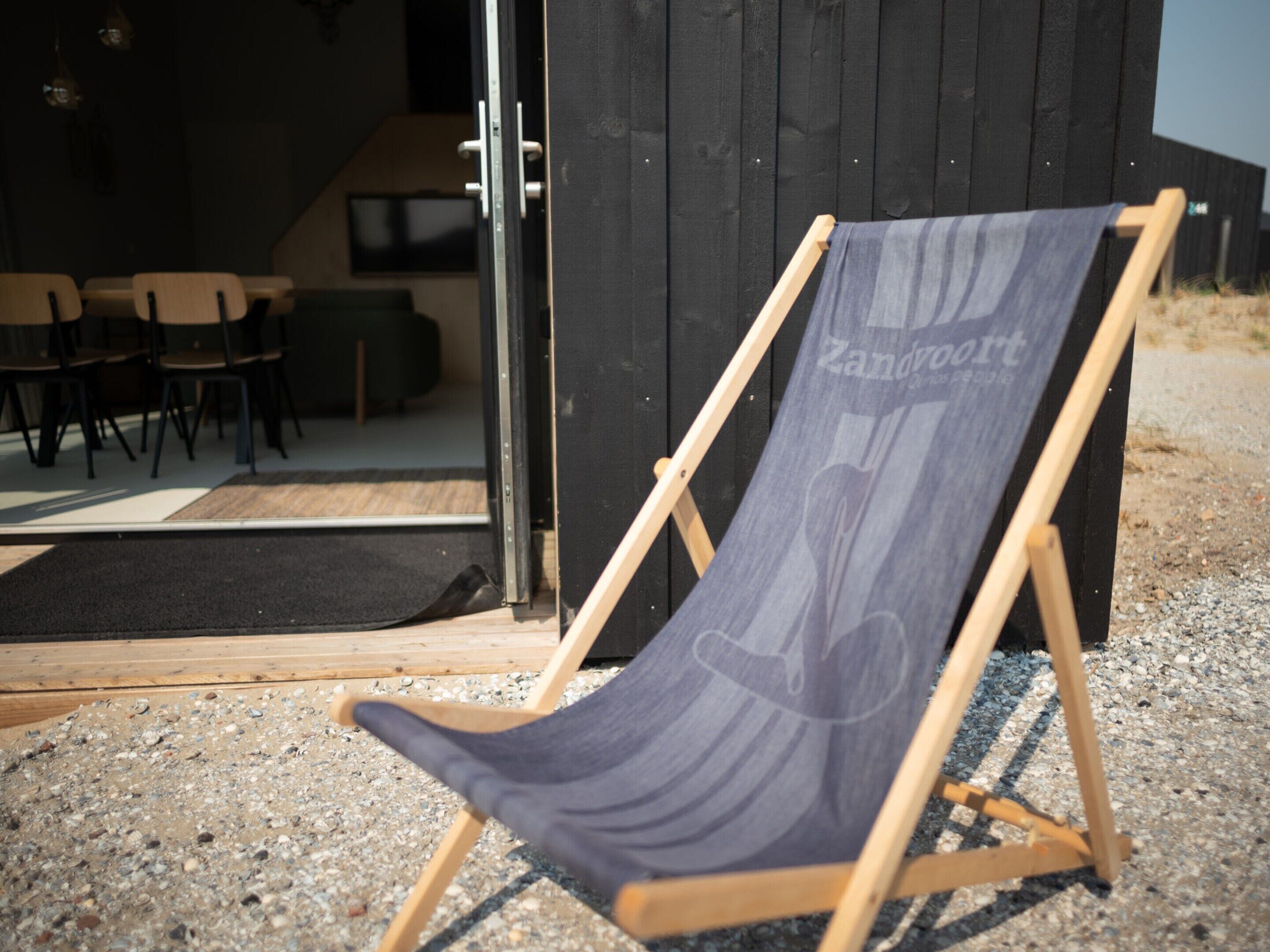 A beach chair with a towel on a wooden stand outside a building with a black exterior.