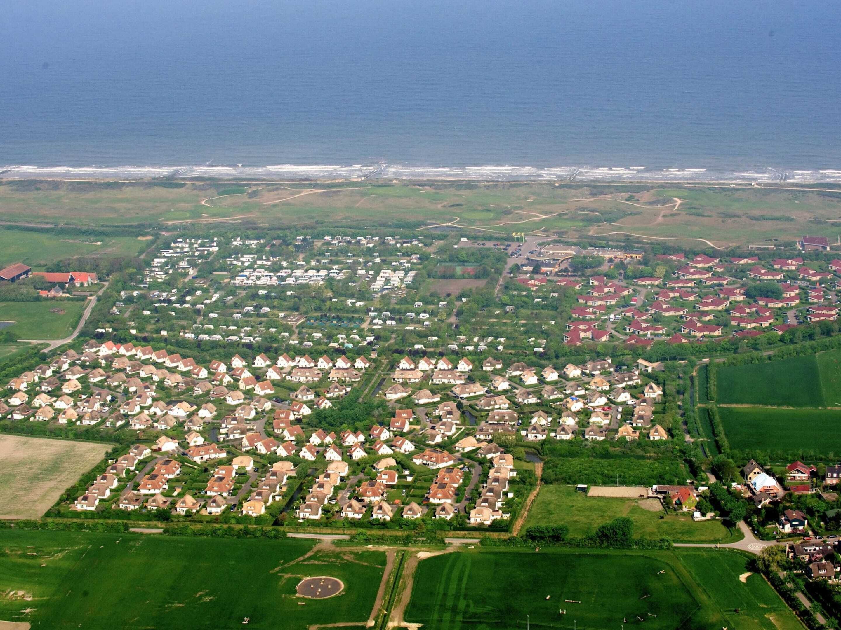 Vue aérienne d’un quartier résidentiel avec des maisons, des champs verdoyants et une côte.
