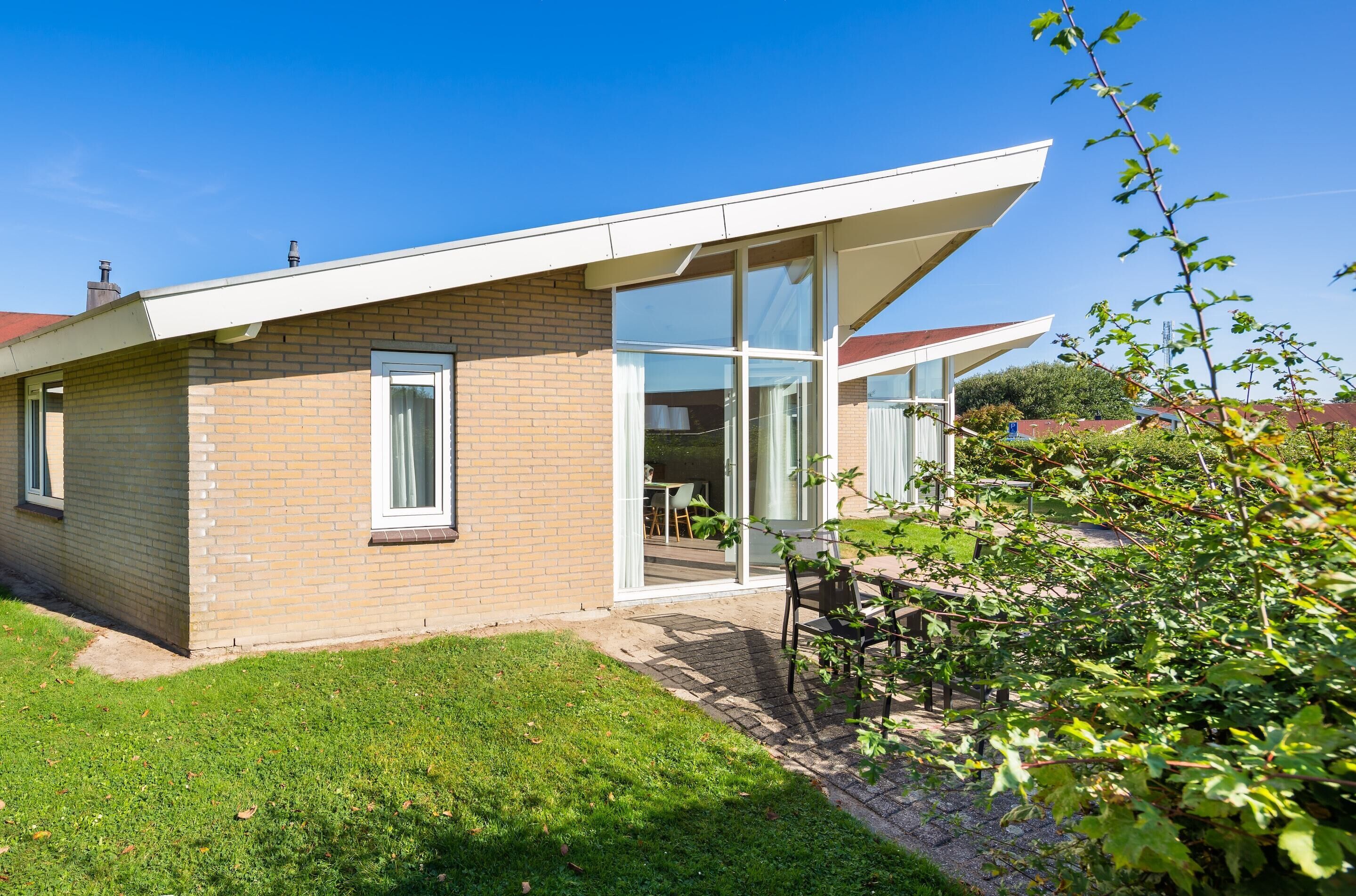 Une maison moderne avec une façade en briques, de grandes fenêtres et une terrasse couverte.