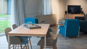 Ein modernes Wohnzimmer mit einem Holztisch, blauen Stühlen, einer Couch und einem Fernseher.
