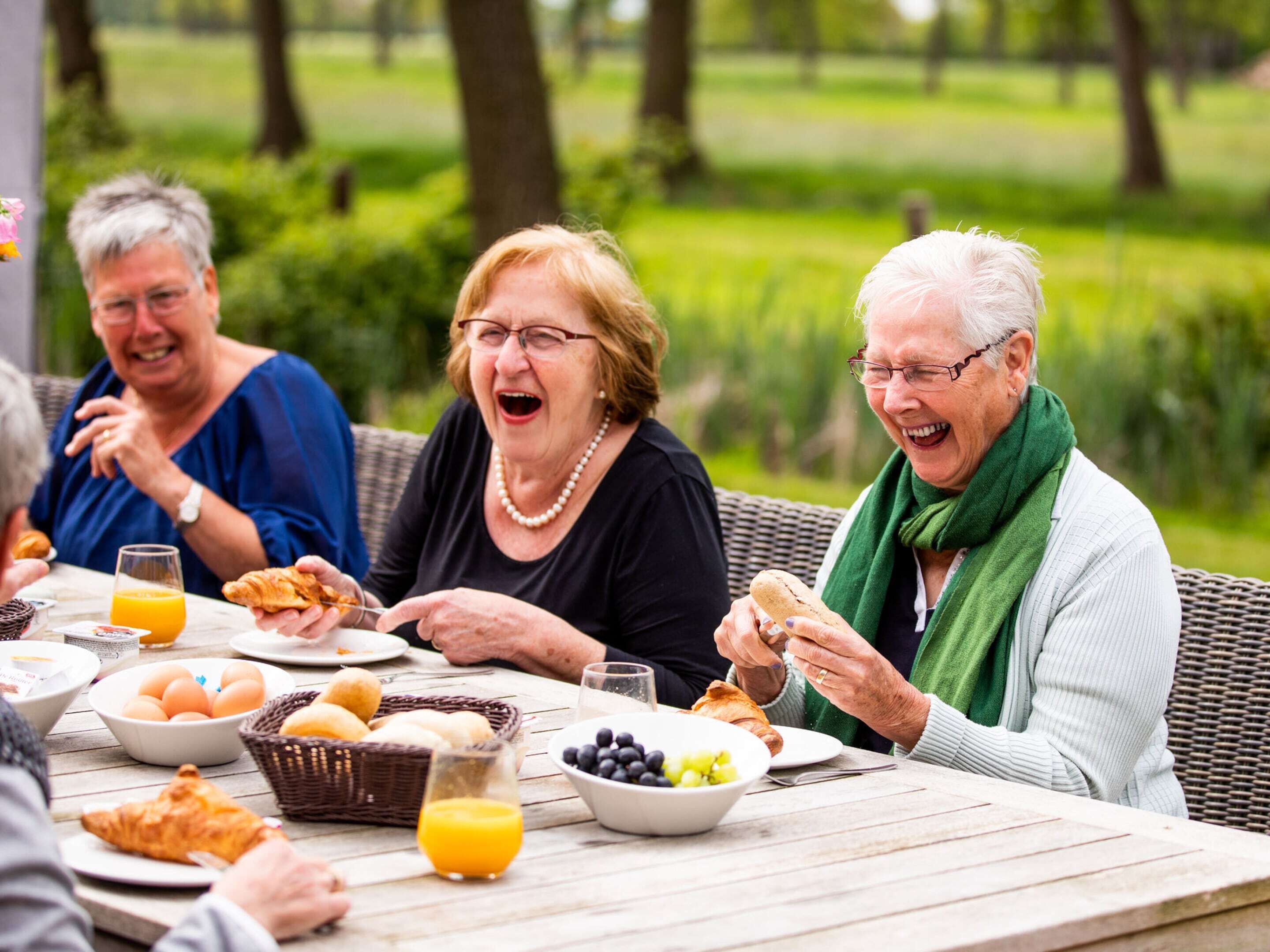 A group of people sitting at an outdoor table with breakfast items like croissants, eggs, and juice.