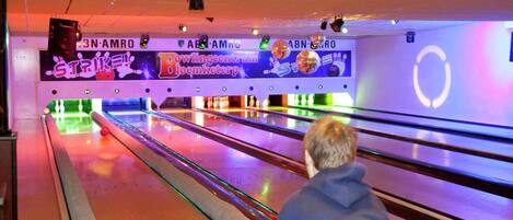 A bowling alley with multiple lanes, a person in a blue hoodie, and neon signage.