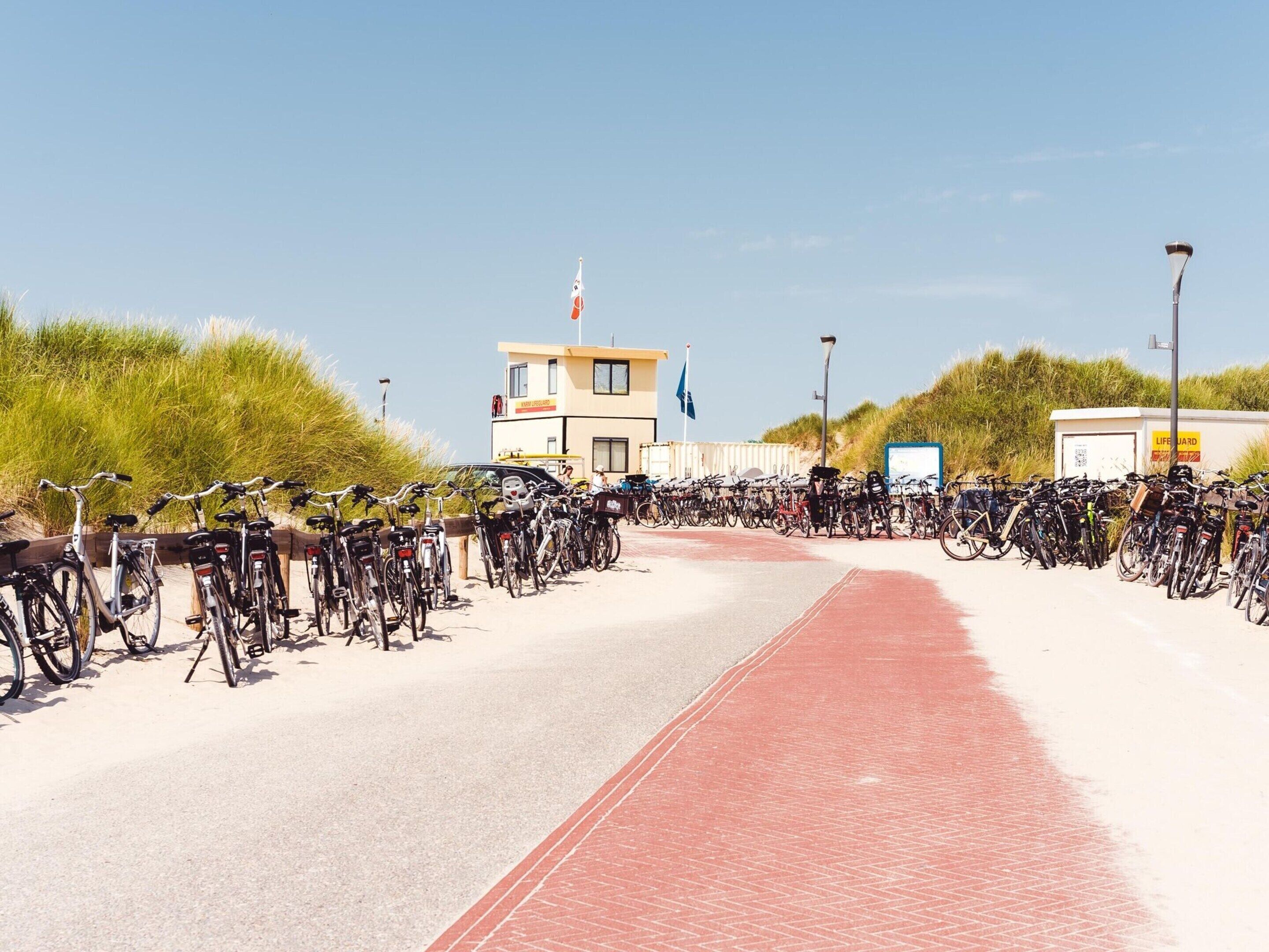 Une zone de location de vélos située sur la côte, avec plusieurs vélos stationnés le long d’un chemin aménagé.