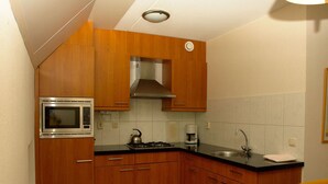 A compact kitchen with wooden cabinets, a built-in microwave, a gas stove, a coffee maker, and a sink.