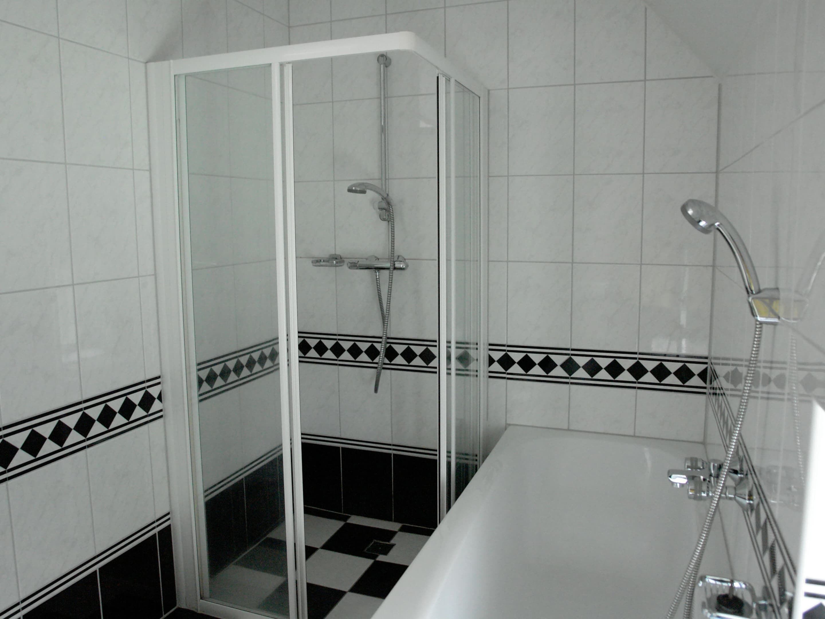 A bathroom with a glass-enclosed shower, a bathtub, and tiled walls with a black and white checkered pattern.
