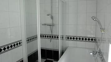A bathroom with a glass-enclosed shower, a bathtub, and tiled walls with a black and white checkered pattern.