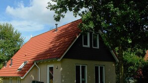 A two-story house with a red-tiled roof, a brick exterior, and a small front porch with a table and chairs.