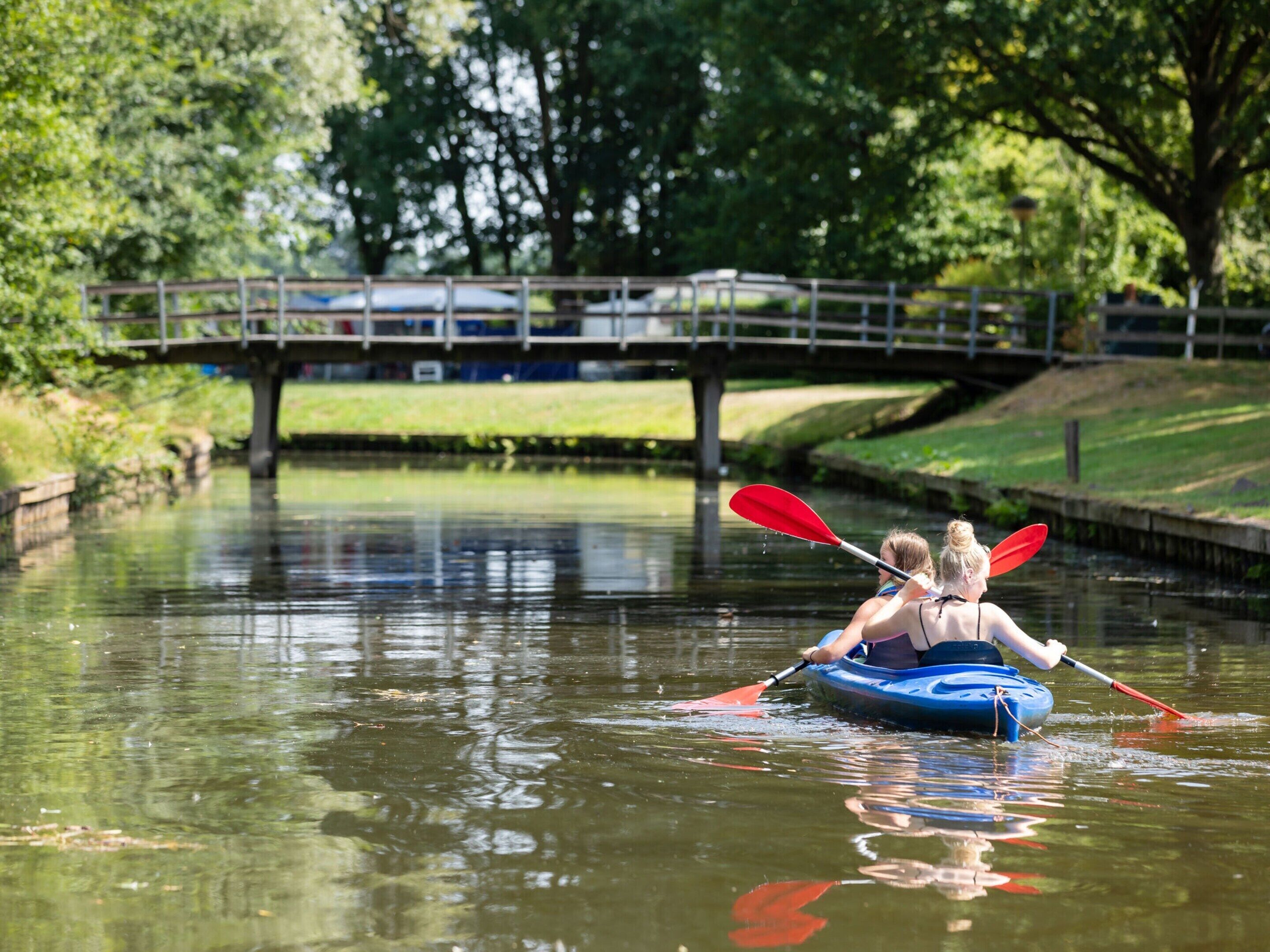Una persona remando en kayak por un río, con un puente al fondo.