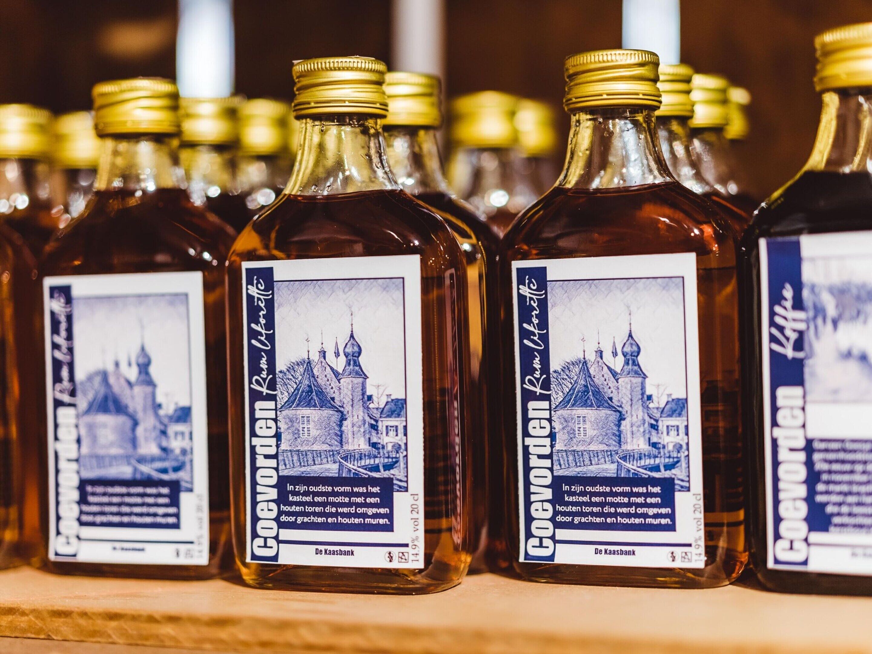 Mehrere Flaschen Coevorden Rumlikör mit Etiketten, die eine blaue Illustration einer Stadt und Text zeigen.