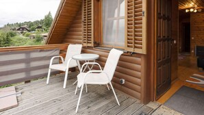 A wooden cabin with a balcony featuring two white chairs and a small table. - Holiday Home in Liebenfels in Carinthia (Liebenfels)