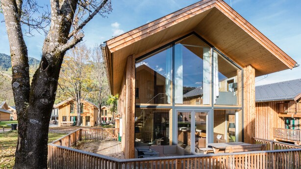 Eine Holzhütte mit großen Fenstern, einer Terrasse und Blick auf den umliegenden Wald.