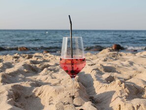 A glass of red drink with a straw on a sandy beach with the sea in the background. - Simplistic Apartment in Kühlungsborn near Beach (Kuehlungsborn)