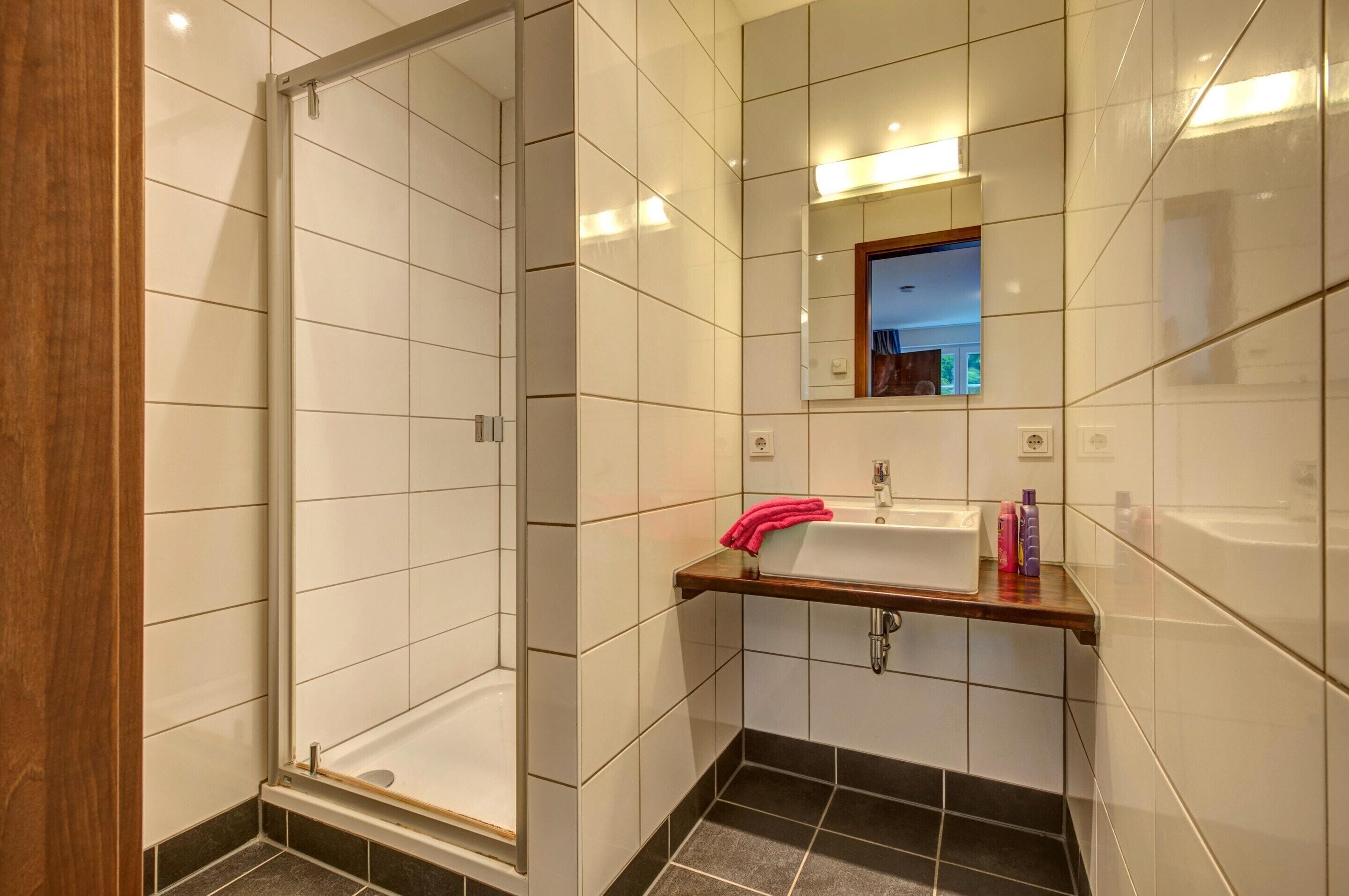 Een moderne badkamer met een douchecabine van glas, een wastafel met een houten aanrechtblad en een spiegel erboven.