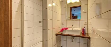 Een moderne badkamer met een douchecabine van glas, een wastafel met een houten aanrechtblad en een spiegel erboven.