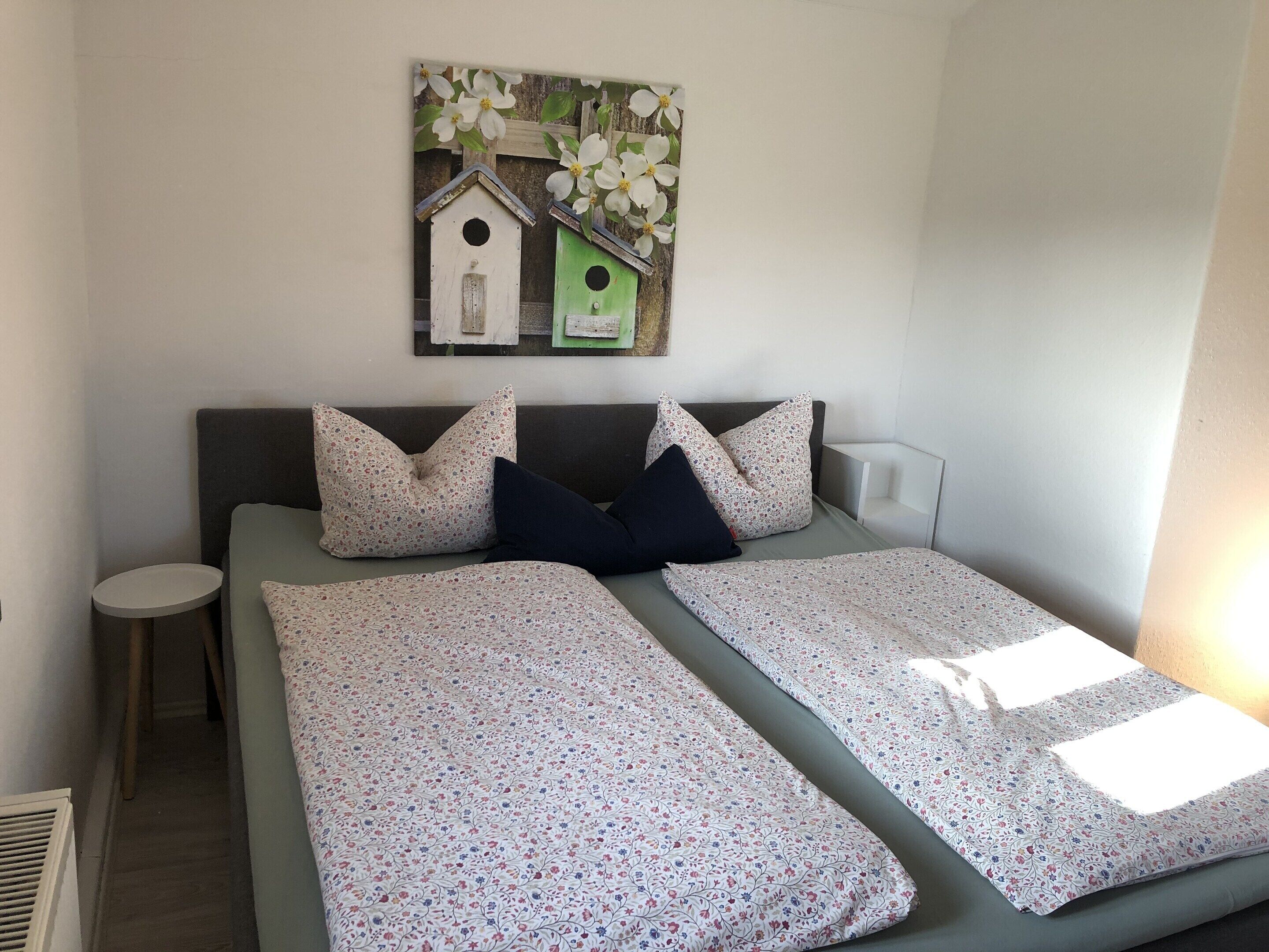 Una cama doble con ropa de cama de estampado floral, una mesita de noche pequeña y una obra de arte en la pared con casas de pájaros.