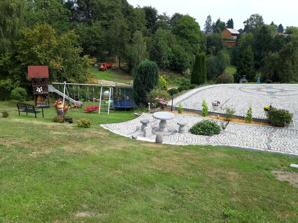 Enjoy a serene outdoor space with a children's play area, birdhouse, and patio seating surrounded by lush greenery.