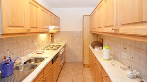 A narrow kitchen with wooden cabinets, a stainless steel sink, and a tiled backsplash. - Spacious Apartment in Schonsee With Sauna (Schoensee)