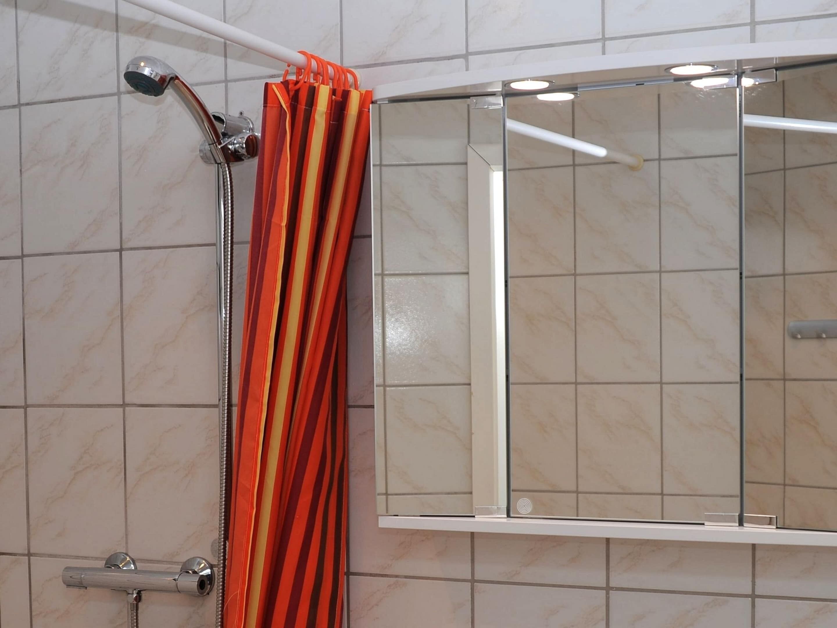 A shower area with a glass enclosure, a handheld showerhead, and a striped shower curtain.