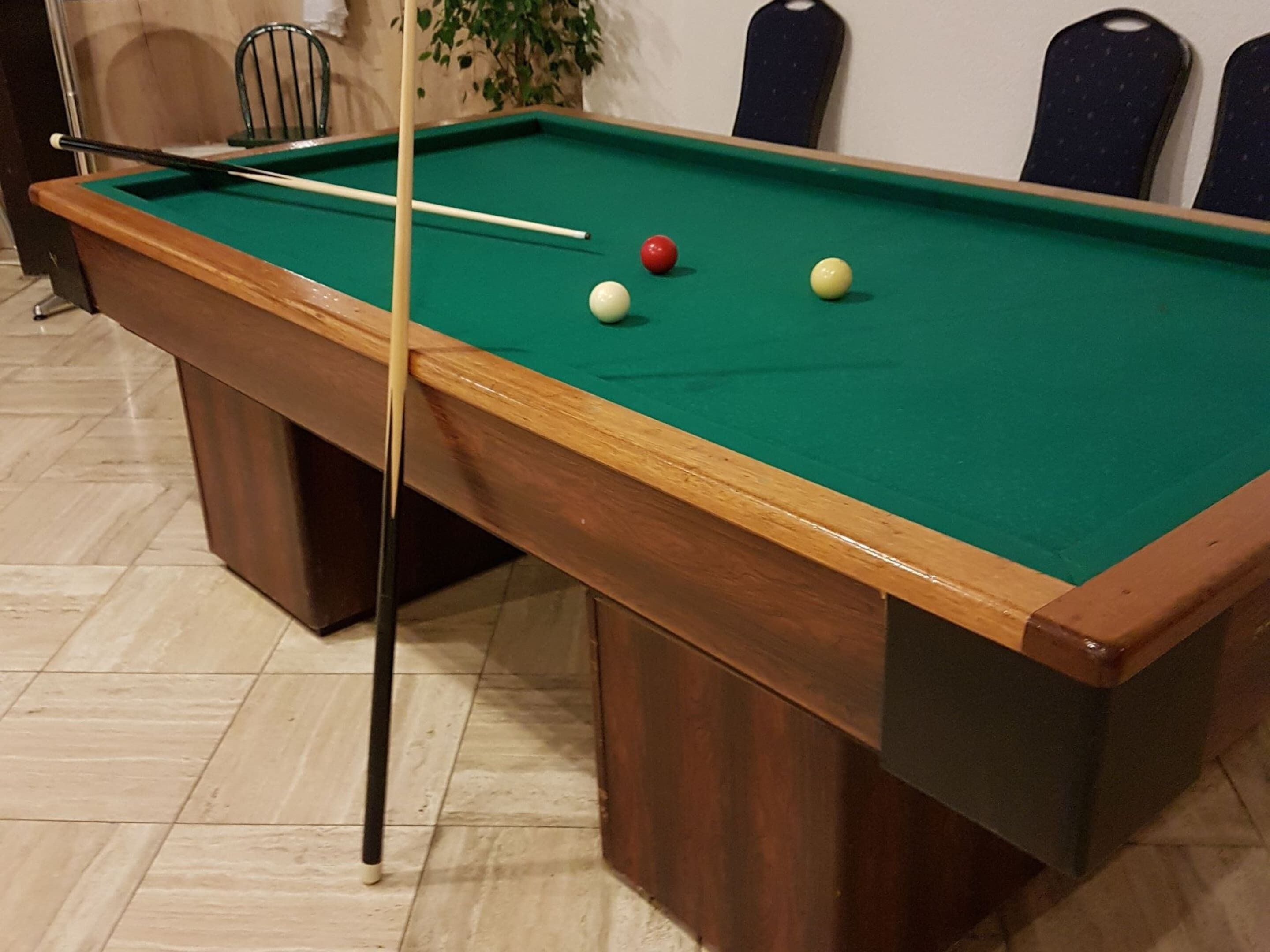 A pool table with a pool cue, two balls, and a chair.