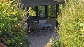 An outdoor patio with a table and chairs, surrounded by dense foliage. - Chalet in Gerolstein Forest Holiday Park (Gerolstein)