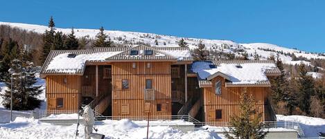 A large wooden chalet with multiple levels, a ski lift, and a snowy mountain backdrop.